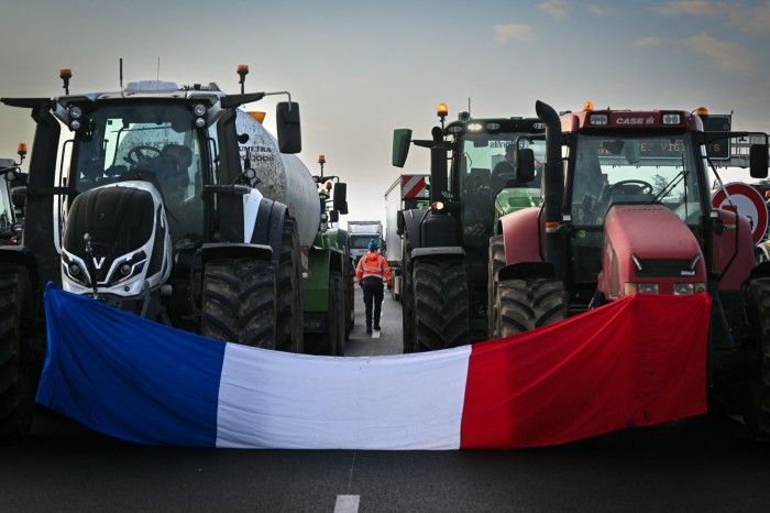 Tractors block a road with a French flag draped in front of them
