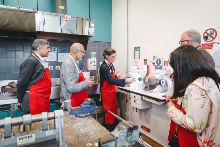 A group of adults wearing red aprons gathered around a workshop machine