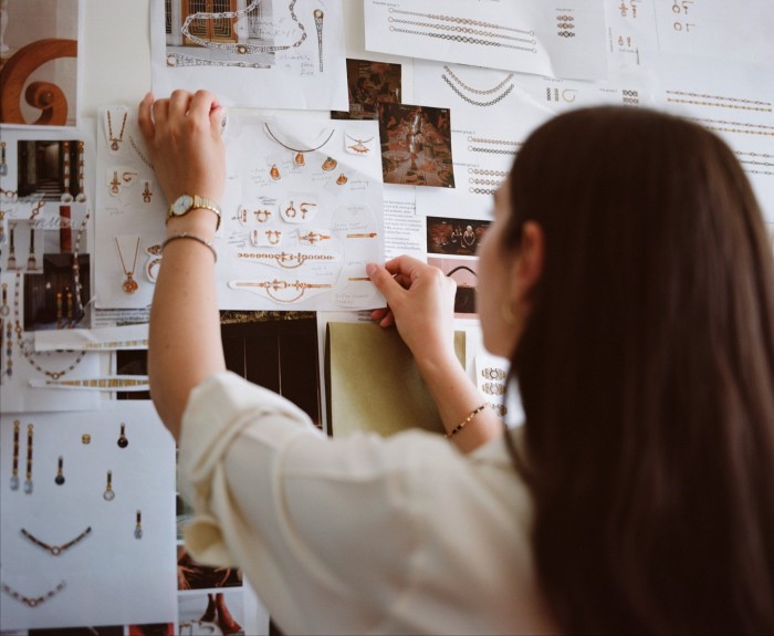 A woman pinning jewellery design sketches on a wall