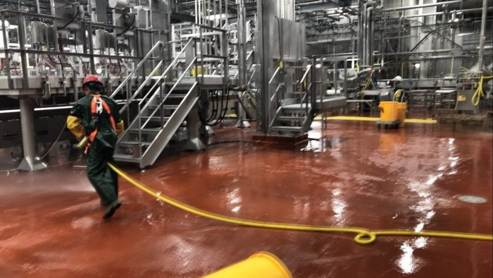 A sanitation worker in protective clothing hoses down machinery and flooring