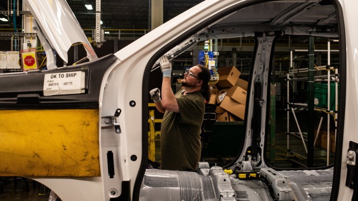 A factory worker inspects the frame of a vehicle on an assembly line