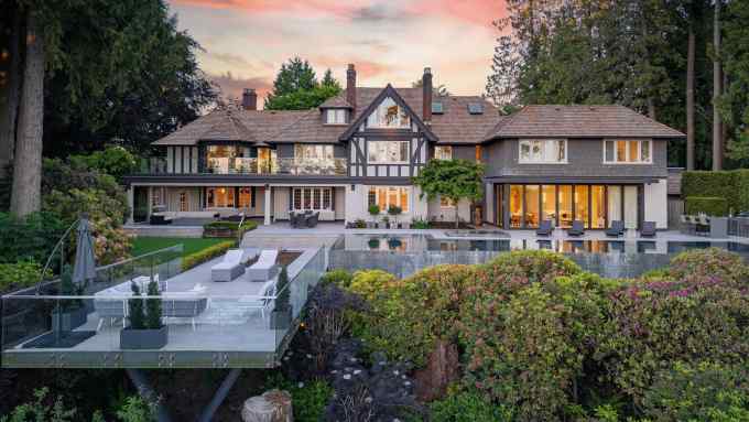 Elegant manor with timber detailing, large terrace, glass balcony, and infinity pool amid vibrant greenery