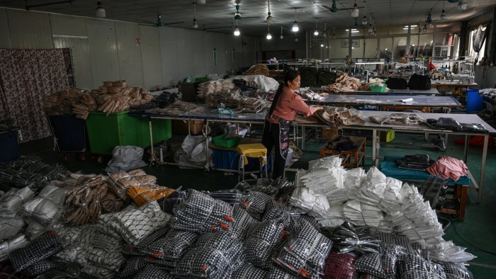 A woman organizes piles of packaged clothing inside a busy garment factory